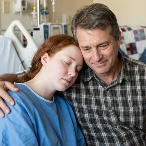 Caring Father with Ill Daughter in Hospital Bed